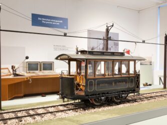 A large scale model of an early Austrian tram displayed on a track with the electric catenary above