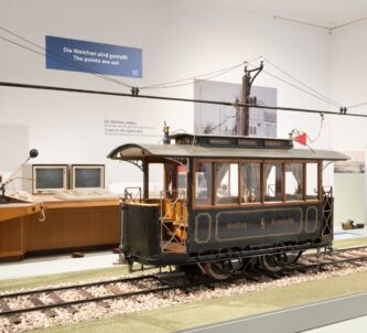 A large scale model of an early Austrian tram displayed on a track with the electric catenary above