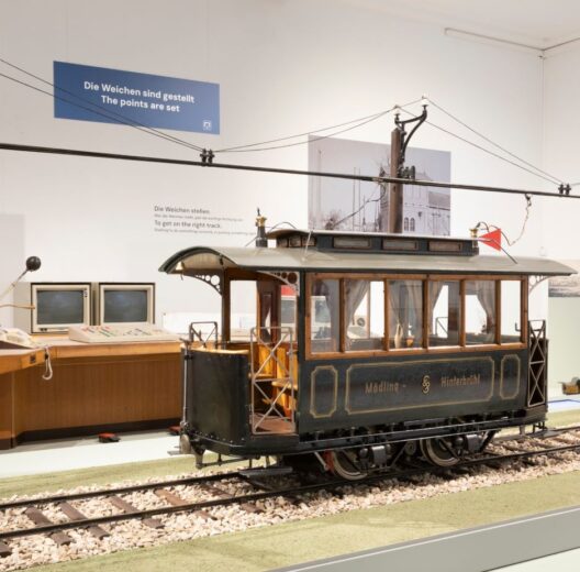 A large scale model of an early Austrian tram displayed on a track with the electric catenary above