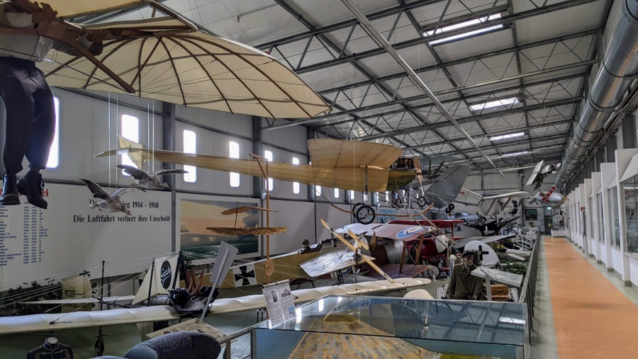 A long hall with classic early aircraft on the floor and suspended in the air