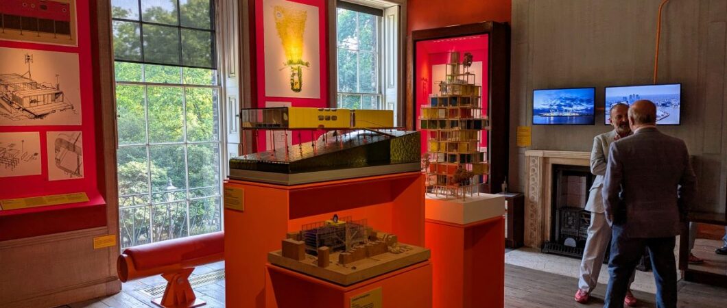 A room with orange info panels on the wall and architectural models displayed in the centre