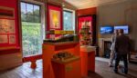 A room with orange info panels on the wall and architectural models displayed in the centre