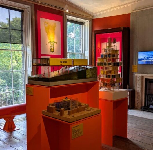 A room with orange info panels on the wall and architectural models displayed in the centre