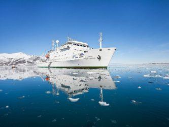 White hulled expedition ship on a dead calm sea surrounded by icebergs