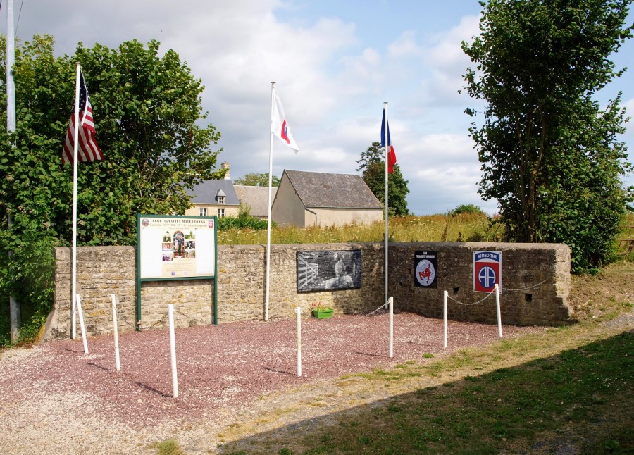 Roadside memorial area for father Maternowski with memorial plaque, info board, flagpoles and a tableau image of him