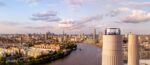 Aerial view of the glass Chimney Lift with people inside at the top of one of Battersea Power Station's chimneys. Behind an below is a panorama of the Thames and London on a glorious sunny day