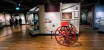 A wooden floored display gallery in the London Museum, Docklands. There are people in the background and a bright red 19th century fire cart in the foreground