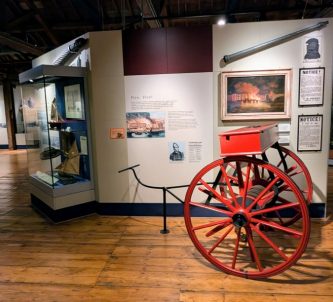 A wooden floored display gallery in the London Museum, Docklands. There are people in the background and a bright red 19th century fire cart in the foreground