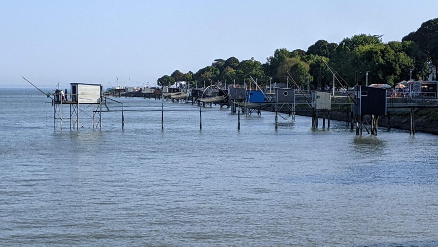 A row of fishing huts on stilts extend out into the bay from the promenade