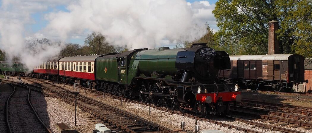 Flying Scotsman steam engine pulling red & white coaches through a small railway junction