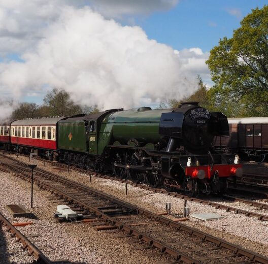 Flying Scotsman steam engine pulling red & white coaches through a small railway junction