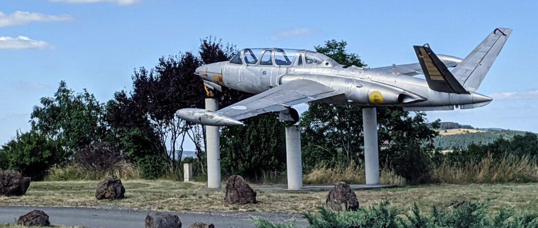 A silver jet aircraft with V-shaped tailplanes sits on three white concrete pillars