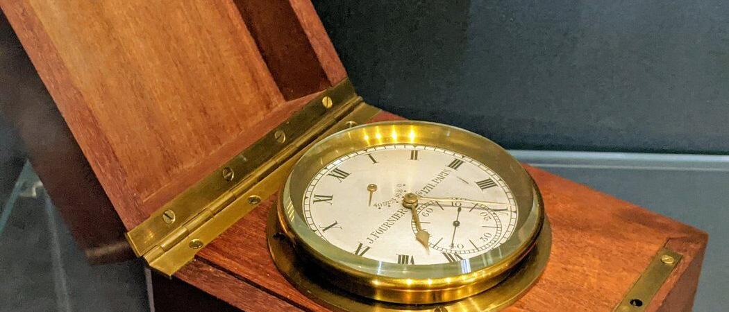 A brass marine clock sits in its varnished wooden box