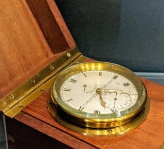 A brass marine clock sits in its varnished wooden box
