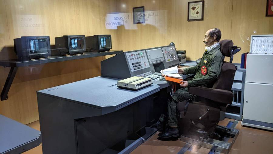 A diorama of an old Cold War control bunker with a moustached mannequin sitting at the desk
