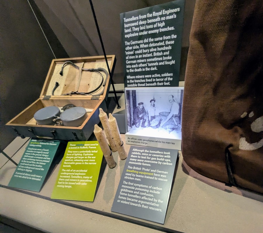 Display case with photos and a wooden box containing what look like two circular grey tins and a stethoscope