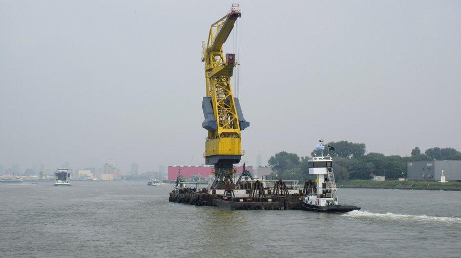 Huge yellow crane-like structure on a barge being pushed by a tug unit