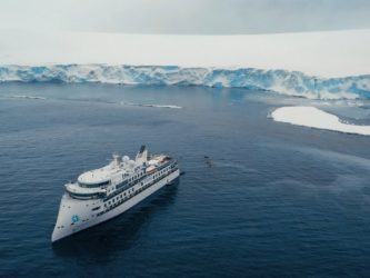 A luxury expedition cruise ship, The Greg Mortimer, floating near an ice laden shoreline
