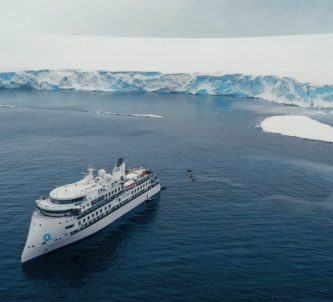 A luxury expedition cruise ship, The Greg Mortimer, floating near an ice laden shoreline