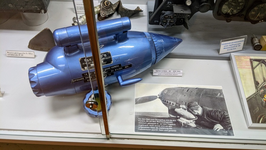 A small gloss blue droplet-shaped device with a photo showing how it bolted to the upper side of the wing above the guns