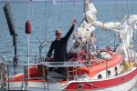 A middle aged yachtsman waves at the camera from the cockpit of his small racing yacht