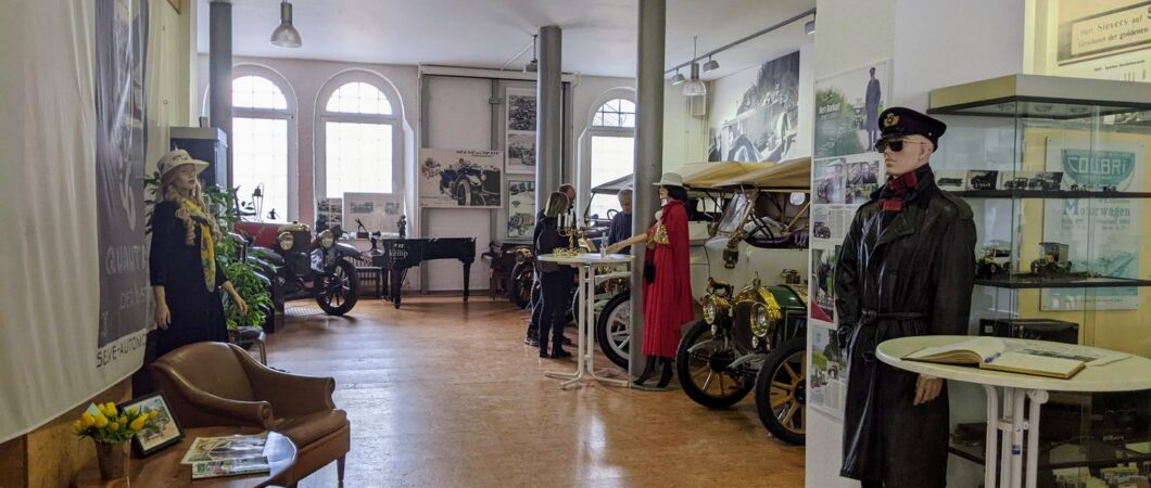 A large hall with classic cars and elegant mannequins in 20th century clothes
