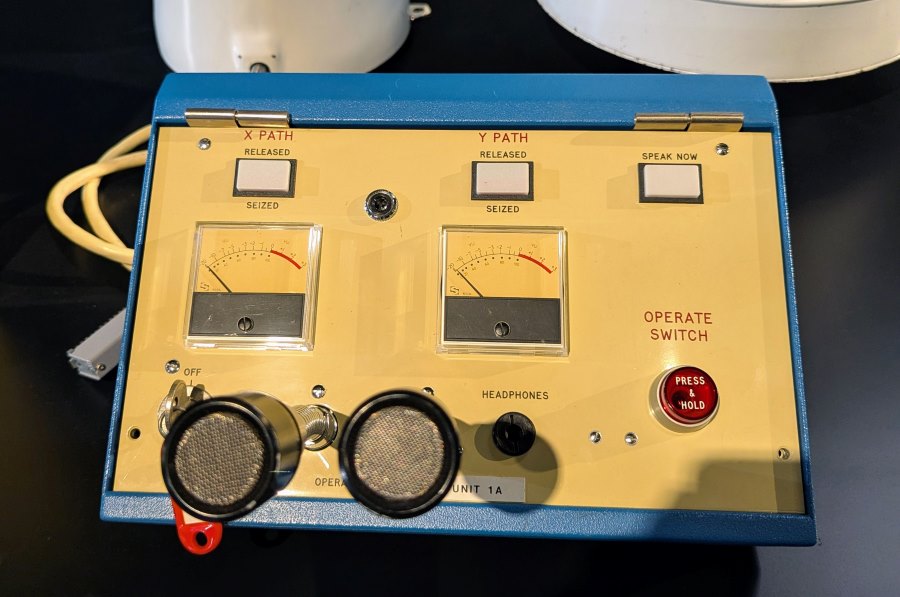 The fascia of an old telecom box with illuminated buttons, selector knobs, meters, and a microphone