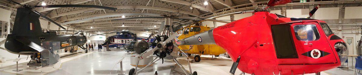 A panoramic view of colourful helicopters on display with a dayglo red helicopter in the foreground