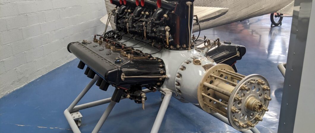 A grey engine with three banks of black cylinders, displayed on an engine stand.