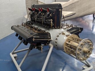 A grey engine with three banks of black cylinders, displayed on an engine stand.