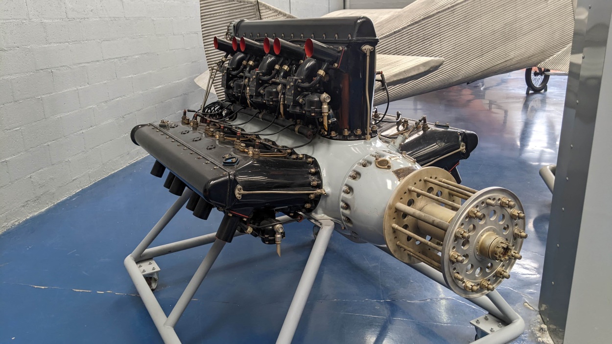A grey engine with three banks of black cylinders, displayed on an engine stand.