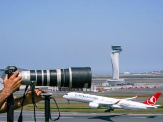 A camera with a telephoto lens overlooks a Turkish Airlines jet taking off at Istanbul Airport with the contral tower in the background