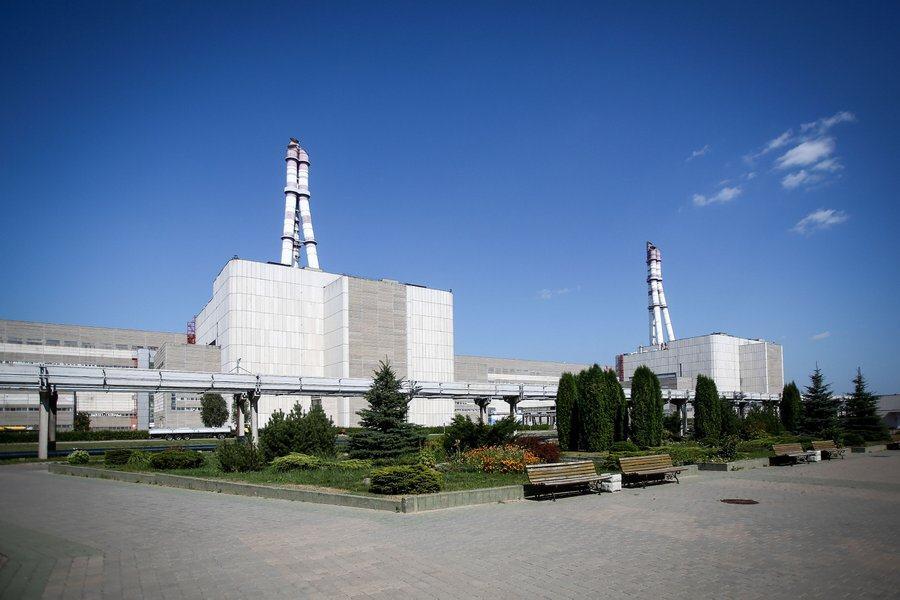 A large white-clad building with no windows and two tripod-like towers on top. There are landscaped gardens in the foreground.