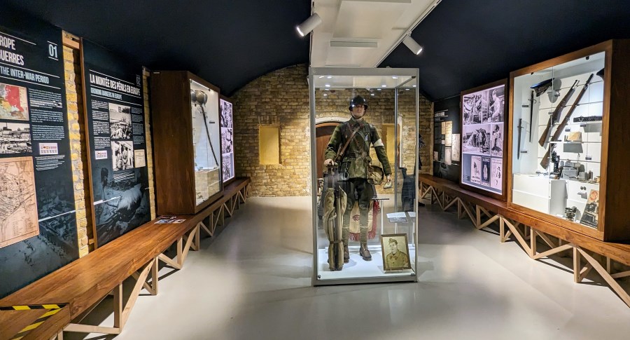 Uniformed soldiers (mannequins) in glass display boxes in a gallery at the Dynamo Museum, Dunkirk. There are info panels and other displays on the walls