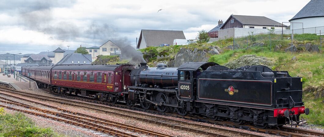 A black K1 class steam engine pulls the vintage red carriages of the 'Jacobite' train, backwards out of Mallaig railway station