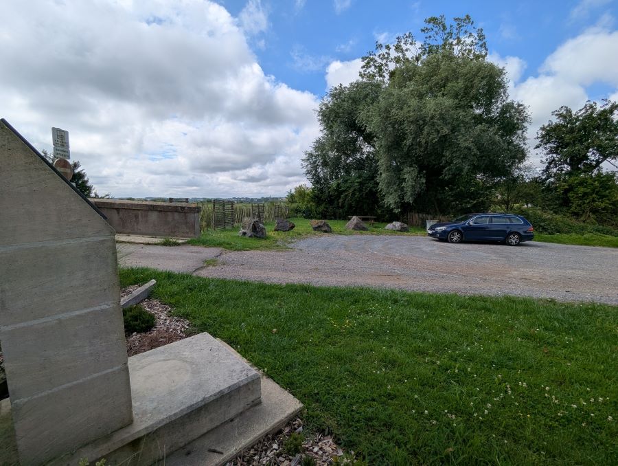 A stone stele in the foreground and a car parked by a picnic are in the background