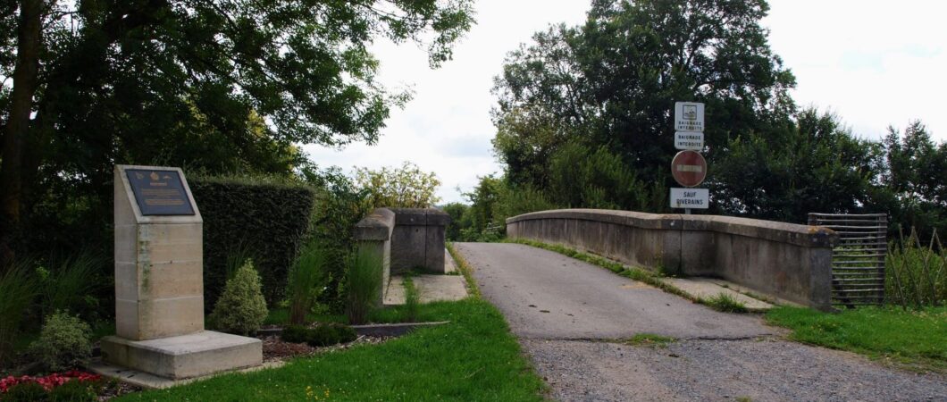 A gravel track leads to a small bridge with a memorial marker stone alongside