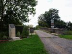 A gravel track leads to a small bridge with a memorial marker stone alongside
