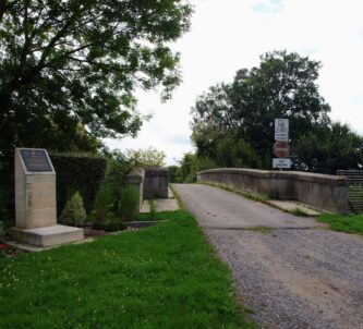 A gravel track leads to a small bridge with a memorial marker stone alongside