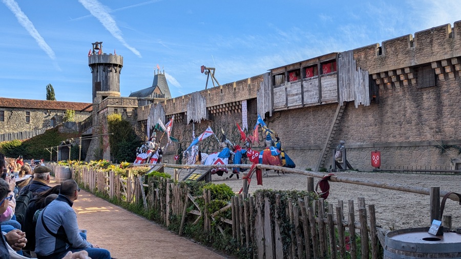 Knights in full regalia ride in a circle in front of a castle wall