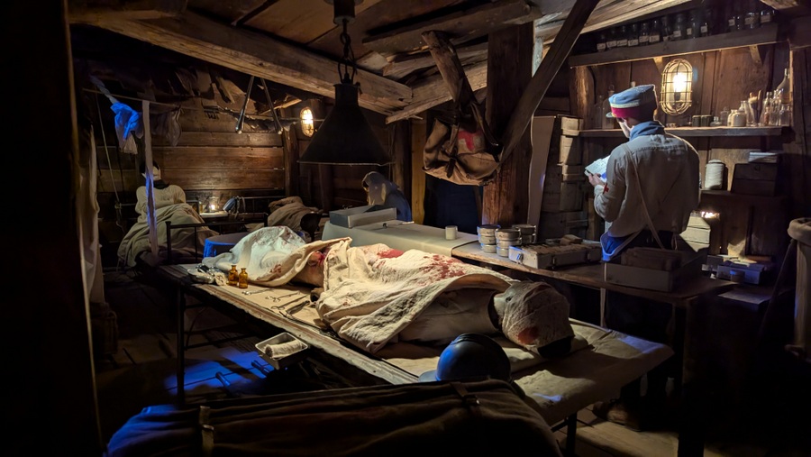 A wounded soldier lies under a sheet on a stretcher while a doctor looks on