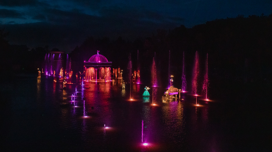 Colourful characters among red lit scenery and fountains on the lake surface