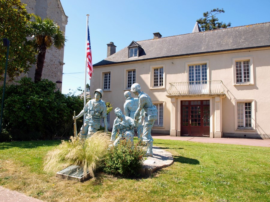 A group of four life-size figures on the grass in front of a pink building