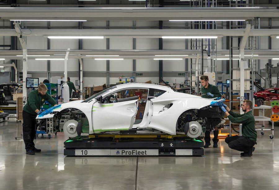 Lotus workers working on a partially-assembled white Lotus Emira sports car
