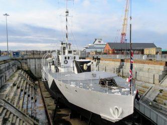 Looking down on a grey and black camouflaged gunboat in a dry dock