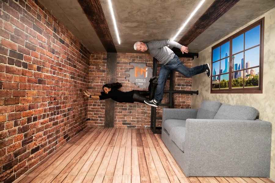 Two people seemingly stand on the side wall of a furnished room