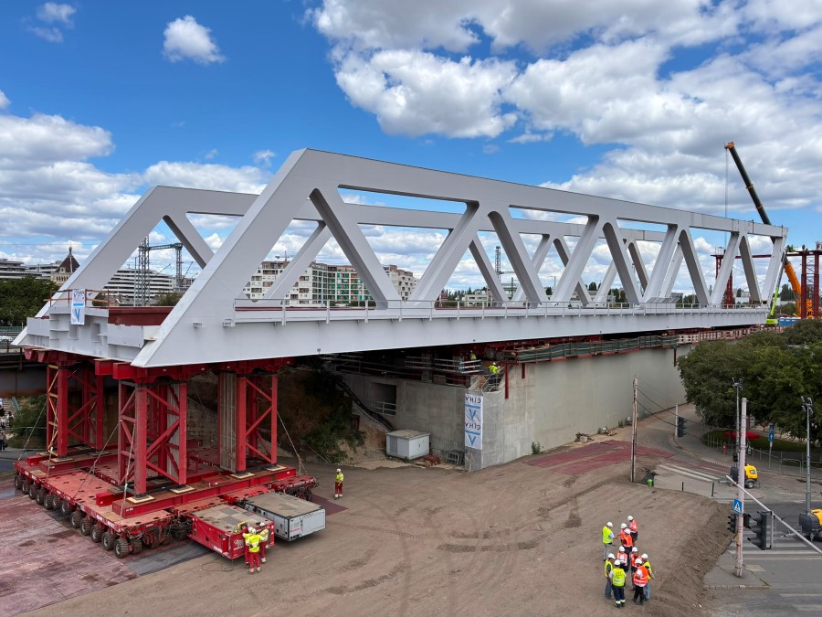 A large grey steel box girder bridge hangs over the gap it is to span