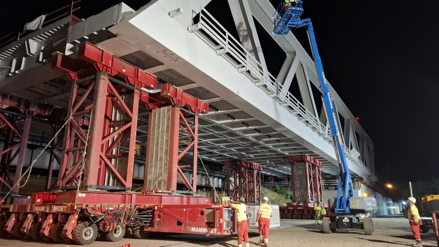 A large grey steel box girder bridge propped up on mobile towers at night