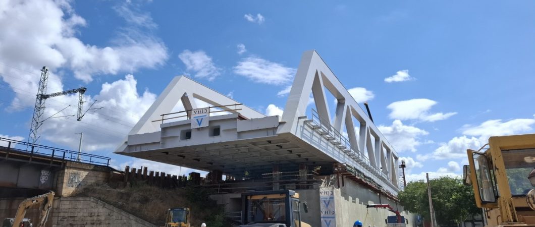 A grey steel box girder bridge span hangs over the road
