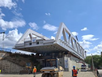 A grey steel box girder bridge span hangs over the road